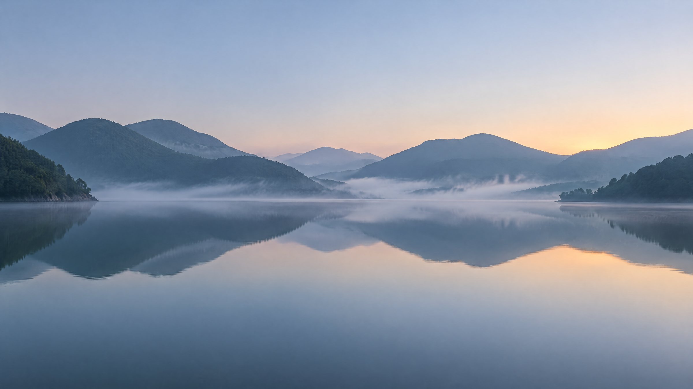 Dawn over a calm bay with low hills and a thin line of mist