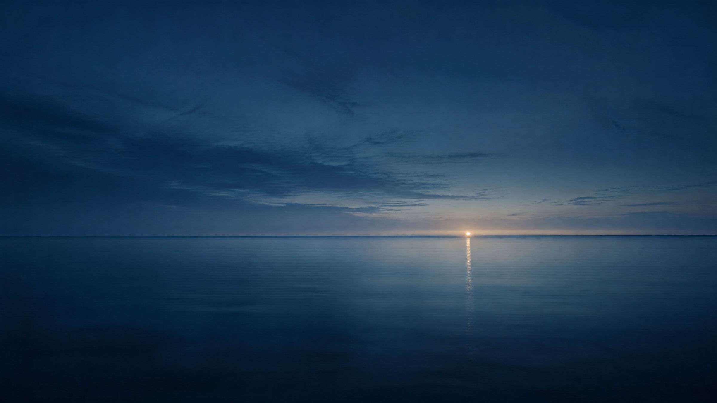 A still sea at blue hour, a low horizon and one soft light on the water